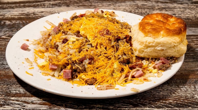 Hearty breakfast skillet with hash browns, eggs, ham, sausage, cheese, and a biscuit.