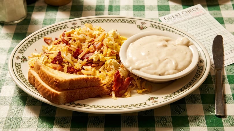 Hearty breakfast plate with scrambled eggs, hash browns, bacon, toast, and a side of gravy.