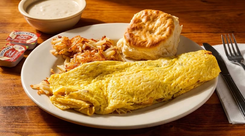 A breakfast plate with a fluffy omelet, crispy hash browns, a biscuit, and gravy.