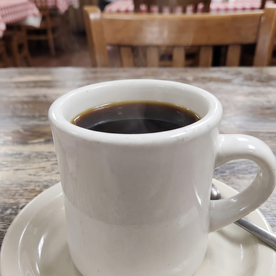 Steaming hot coffee in a white mug on a rustic wooden table with a sugar caddy.